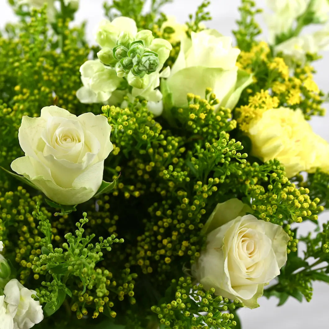 Bouquet of white and yellow roses with greenery on a light gray background