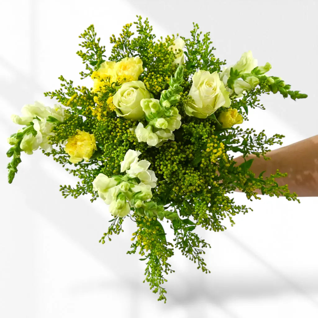 Bouquet of green and yellow flowers held by a hand on a white background