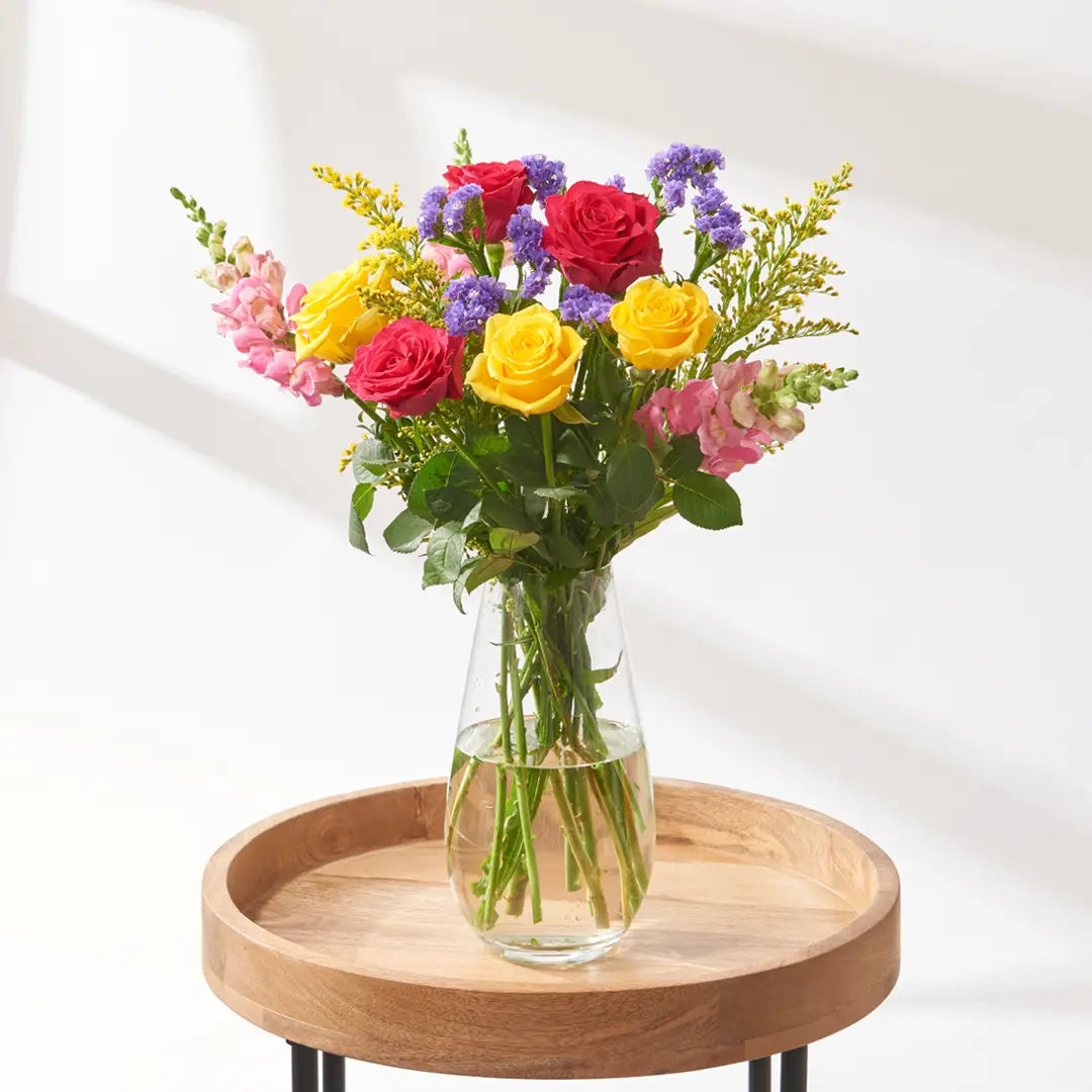 Red and yellow rose bouquet with purple statice, pink snapdragons and yellow solidago in glass vase