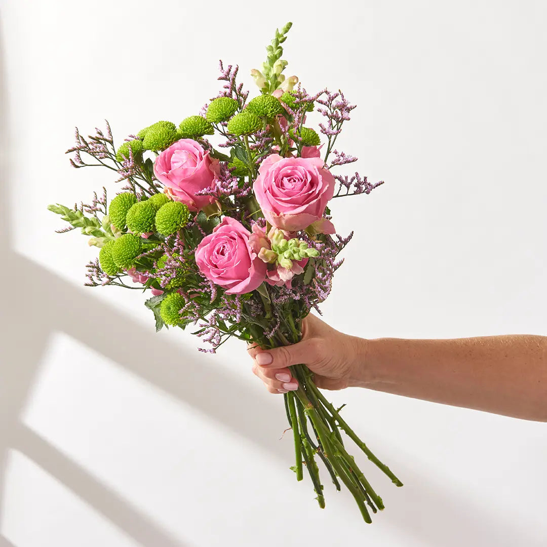 Hand holding pink roses with green Santini, pale antirrhinum and purple limonium stems