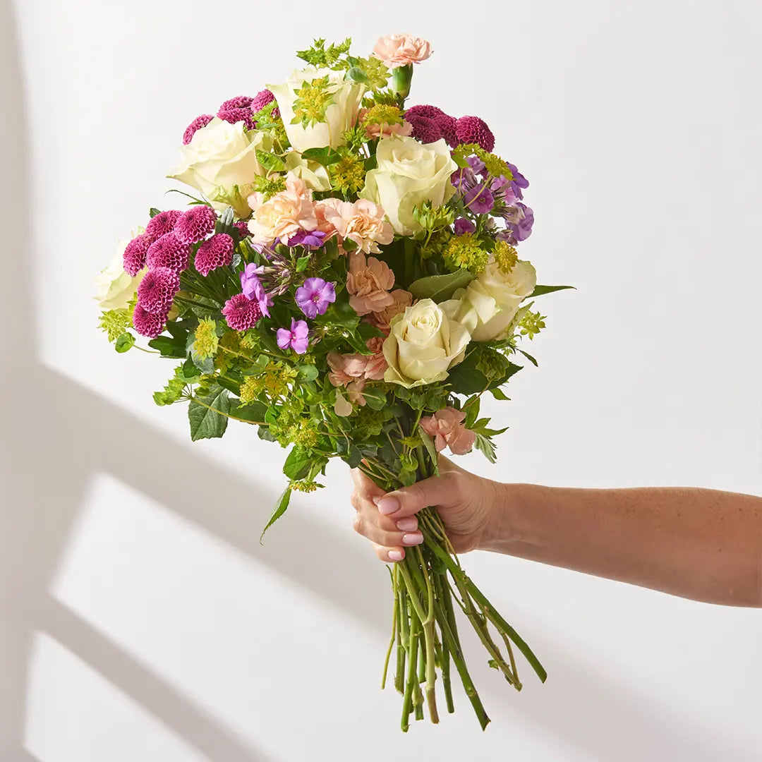 Hand holding a fifteen stem multi colour mixed flower bouquet with white roses showing stem length and scale