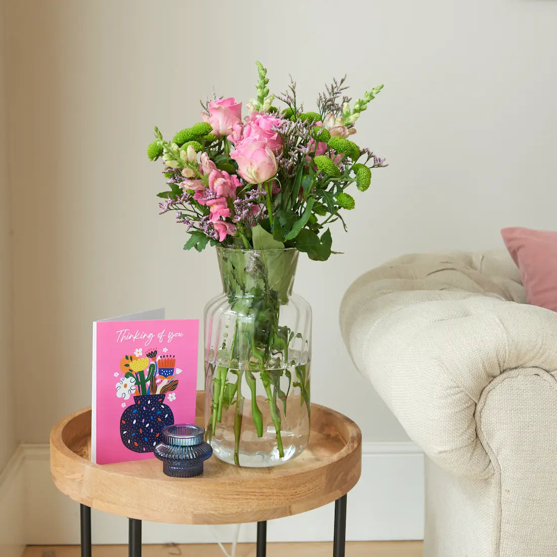 Pink roses and green Santini in glass vase beside pink “Thinking of you” card