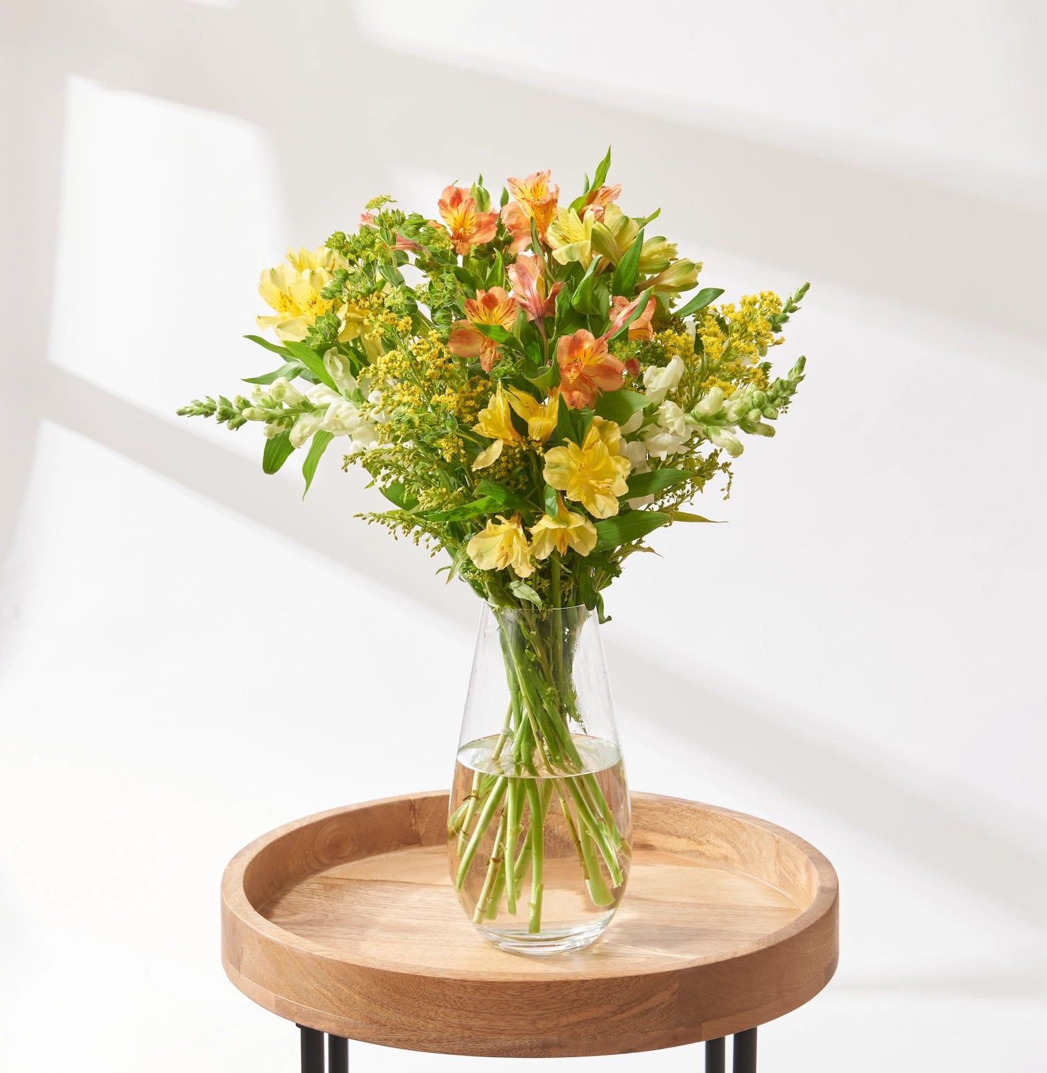 Yellow and peach mixed flower bouquet with alstroemeria, solidago, white antirrhinum and bupleurum arranged in a clear glass vase